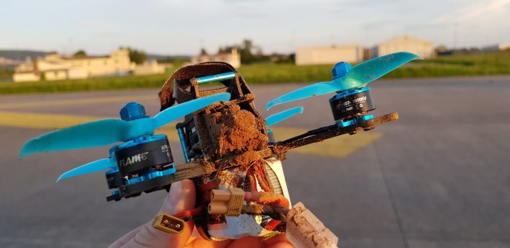 FPV drone with blue propellers submerged in the dirt.