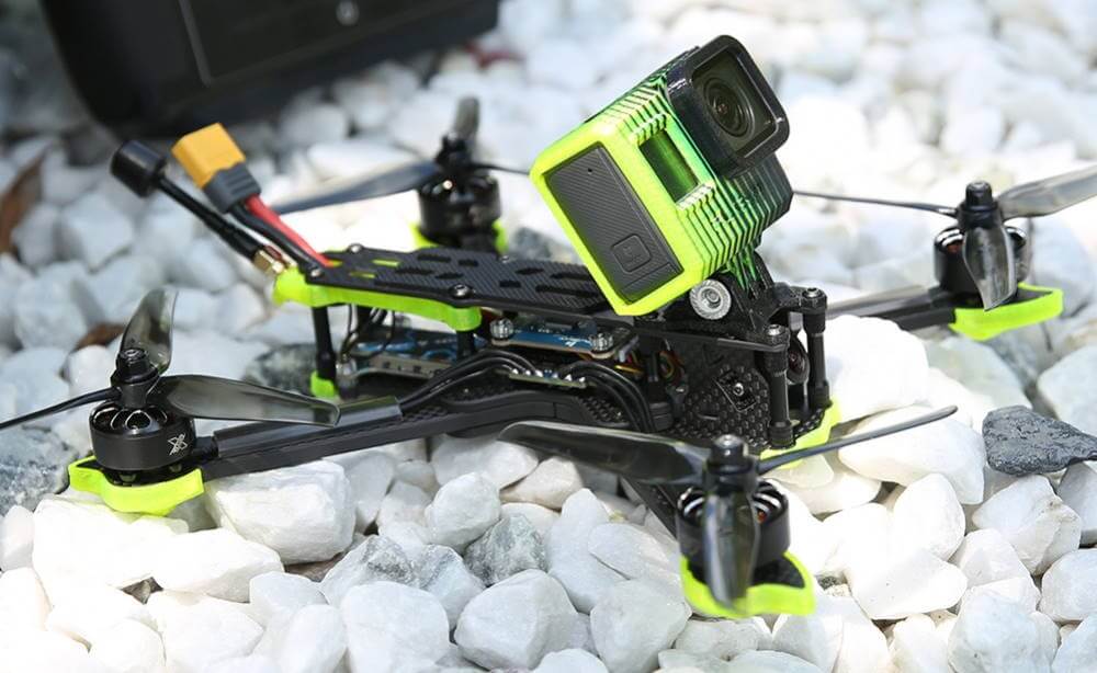 Black and green colored FPV drone on white pebbles.